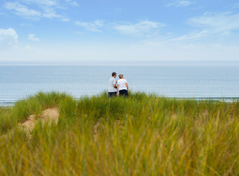 Stay with Us. Elderly couple on the sand dunes at Croyde Bay looking out to sea.