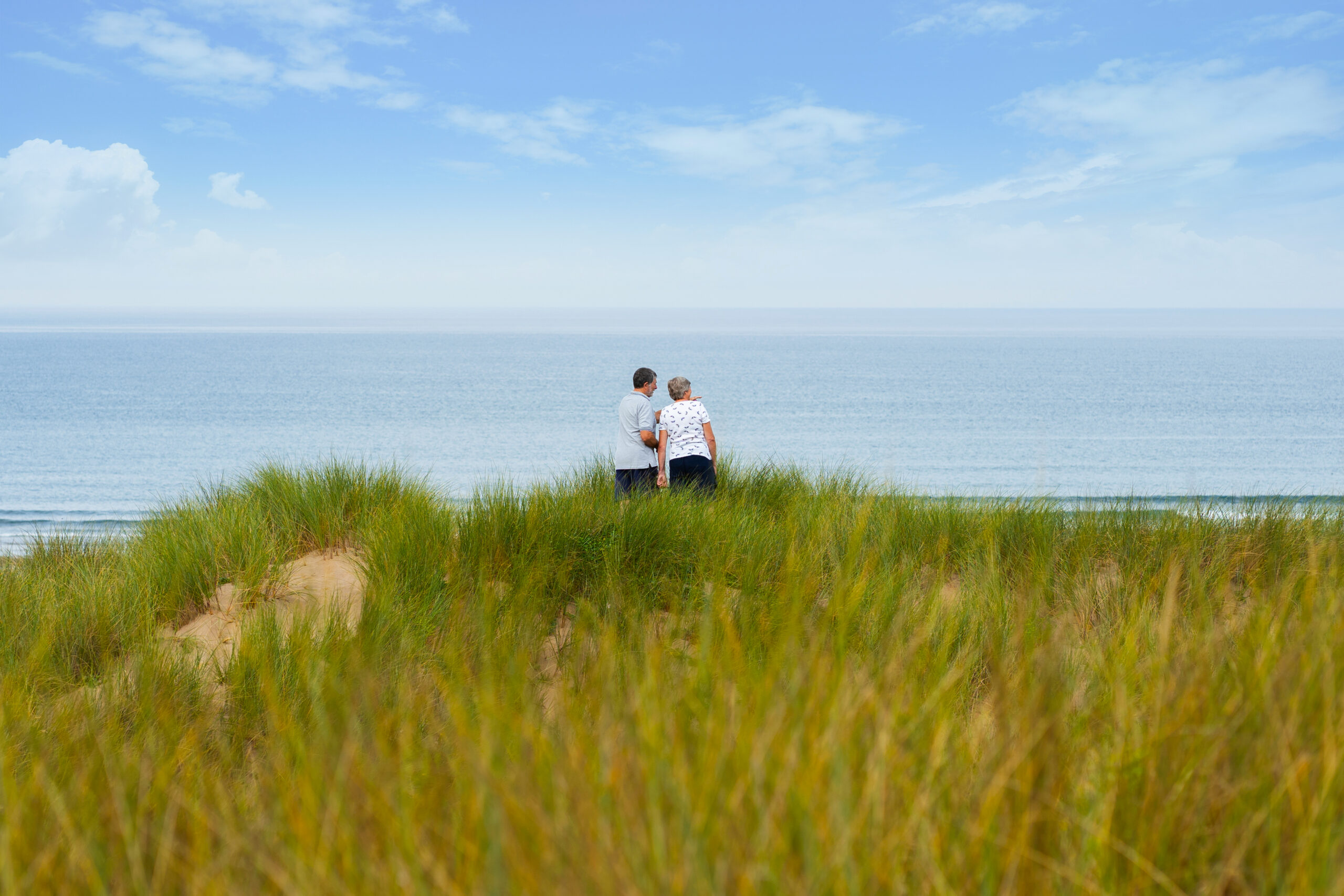 Stay with Us. Elderly couple on the sand dunes at Croyde Bay looking out to sea.